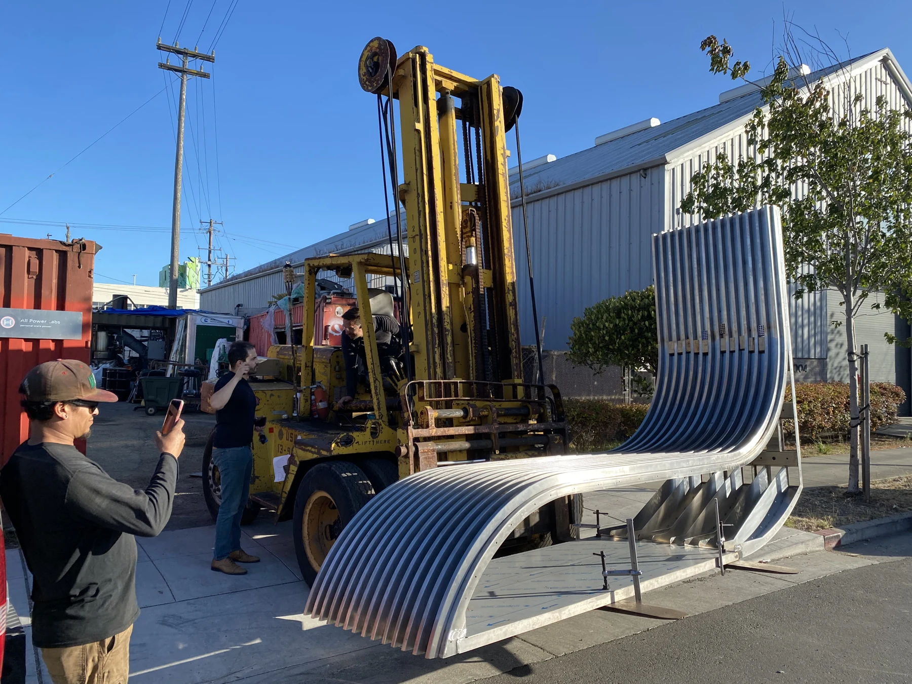 Fabricated curved metal assembly being handled outdoors, matching the adjacent CAD model